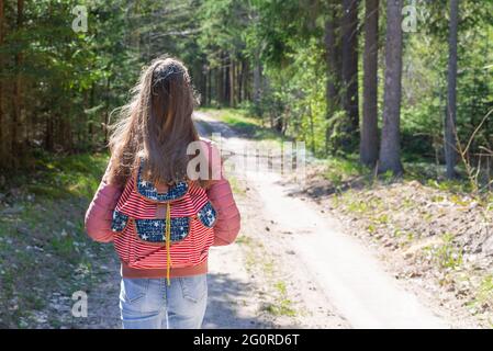 Ein junges Mädchen mit Rucksack zu Fuß entlang Weg durch den Wald während des Sommers. Hipster Lifestyle und Solo Trip.Rückansicht. Stockfoto