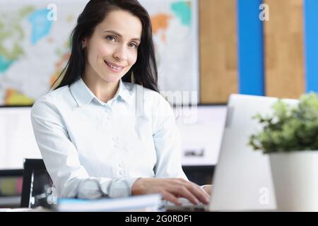 Eine junge lächelnde Geschäftsfrau sitzt im Büro am Laptop Stockfoto