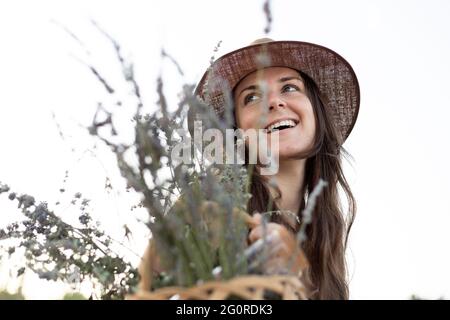 Porträt einer jungen Frau, die einen Korb mit wilden Blumen in der Hand hält und nach oben schaut. Weichfokus Stockfoto
