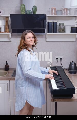 Frau schwanger Musiker steht in der Küche zu Hause in der Nähe des digitalen Klaviers Stockfoto