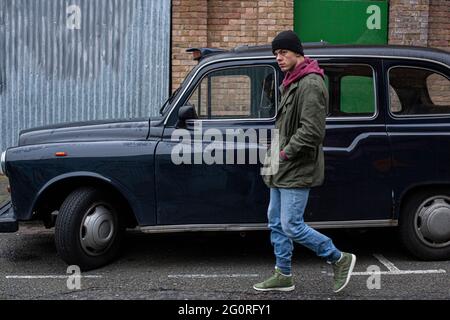 Mann, der an einem leeren schwarzen Taxi auf einer Straße in London vorbeifährt.Alte verlassene Taxis auf den Straßen Londons, Stockfoto