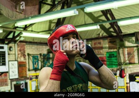 Junger Mann, der Boxkopfwächter aufsetzt und sich für das Boxtraining im Boxclub vorbereitet Stockfoto