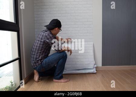 Junge asiatische Mann kleben Tapeten an der Wand zu Hause. Renovierungsraum im Haus von selbst diy-Konzept Stockfoto