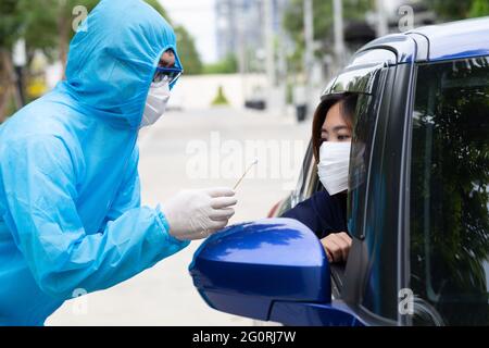 Krankenschwester mit PSA-Anzug oder medizinisches Personal in voller Schutzausrüstung nimmt die Probe von der Fahrerin im Auto. Drive-Thru-Test für Coronavirus COVID Stockfoto