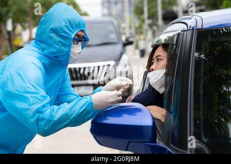 Krankenschwester mit PSA-Anzug oder medizinisches Personal in voller Schutzausrüstung nimmt die Probe von der Fahrerin im Auto. Drive-Thru-Test für Coronavirus COVID Stockfoto