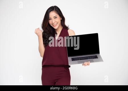 Porträt einer aufgeregten asiatischen Frau, die ihren Laptop hält und den Erfolg auf weißem Hintergrund feiert und die Arme mit einem glücklichen Blick hebt, femal Stockfoto