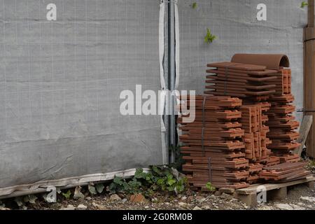 Dachziegel gebündelt und auf einer Holzpalette auf einer Baustelle platziert. Auf dem Hintergrund befindet sich Platz für Kopien. Stockfoto