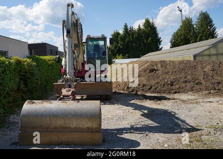 Rot-weißer Bagger mit Taucheimer, der auf der Baustelle in der Nähe des Abgrunds mit Bäumen, Glashaus und blauem Himmel im Hintergrund geparkt ist. Stockfoto