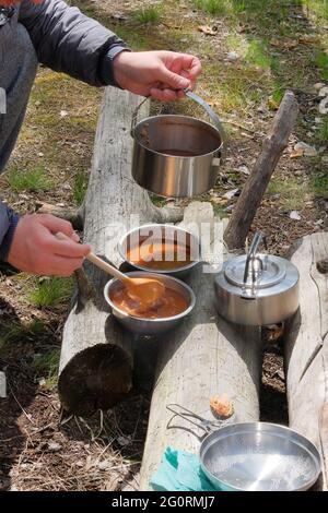 Touristische Küche für Outdoor-Aktivitäten. Suppe in Schüsseln auf Holzstämmen im Wald. Camping Lebensmittelherstellung. Stockfoto