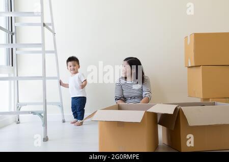 Asiatische Mutter und Baby Junge mit Pappkartons im neuen Haus am Umzugstag, Immobilien und Hausfamilie Konzept Stockfoto