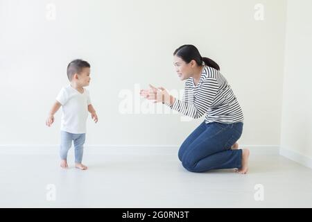 Asiatische Baby junge lernen zu gehen mit beobachten und kümmern sich von Mutter, Sohn nehmen die ersten Schritte zu Hause Stockfoto