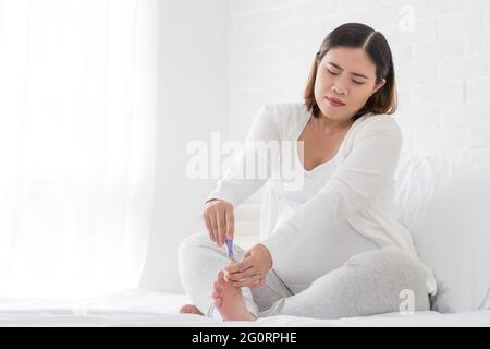 Schwangere Frau schneiden Nägel Füße von nail Clipper auf weißen Bett im Schlafzimmer, Schönheitsbehandlungen für Fuß- und Nagelpflege und Maniküre während der Schwangerschaft Stockfoto