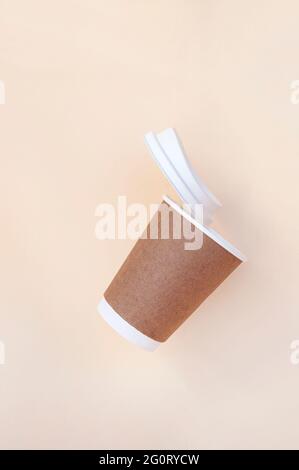Braune Kaffeetasse aus nachhaltigem Papier und weißer Papierdeckel auf beigefarbenem Hintergrund. Zero Waste Konzept. Stockfoto