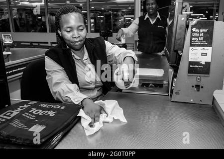 KAPSTADT, SÜDAFRIKA - 06. Jan 2021: Kapstadt, Südafrika - 23. März 2020: Kassierer, die an der Kasse arbeiten, wischen Oberflächen in Pick 'n Pay Lebensmittelgeschäften ab Stockfoto