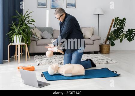 Sanitäter demonstrieren erste Hilfe an Übungspuppe während des Trainings allein im Wohnzimmer. Der Ausbilder zeigt die HLW an der Trainingspuppe Stockfoto