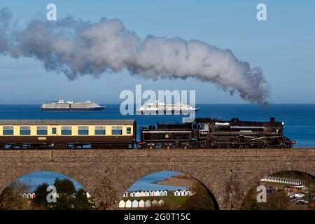 Ein Zug der Dartmouth Steam Railway Linie fährt am Viadukt von Broadsands entlang, während die Oosterdam & Volendam-Schiffe sich in der herrlichen Sonne sonnen Stockfoto