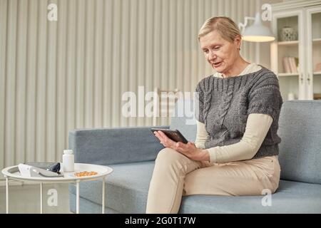 Kranke ältere Frau während eines Videoanrufs mit einem Arzt. Seitenansicht eines Patienten, der sich während einer Telefonkonferenz mit seinem Arzt in Quarantäne befindet. Stockfoto