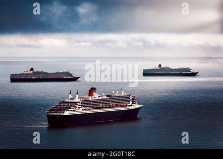 Drei Queens ... L-R: Queen Elizabeth, Queen Mary 2 & Queen Victoria Kreuzschiffe sind nebeneinander abgebildet, während sie vor Torbay, Devon, vor Anker liegen. Stockfoto