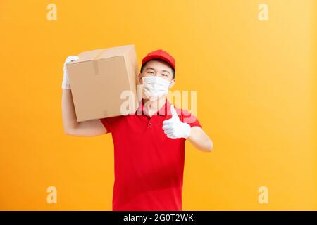 Sichere Lieferung. Frau Courier in schützender Gesichtsmaske und Handschuhen mit Karton-Box. Anti-Coronavirus-Konzept. Stockfoto