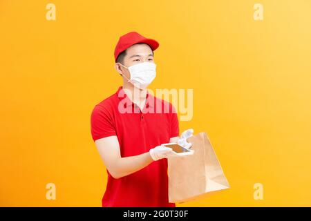 Junger gebender Mann mit medizinischen Handschuhen und Schutzmaske, der Smartphone mit Kopierraum und Einkaufstaschen in den Händen hält. Stockfoto