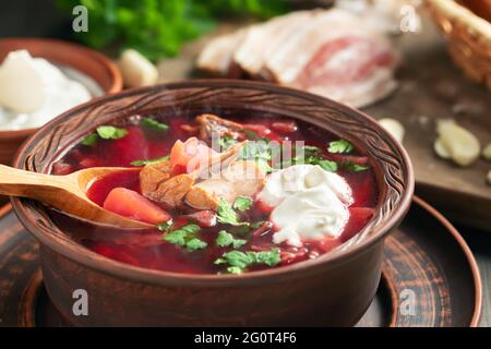 Frisch gekochtes Borscht: Traditionelles Gericht der russischen und ukrainischen Küche in Steingutgerichten mit Speck, Brot, Sauerrahm und Knoblauch, Nahaufnahme. Stockfoto