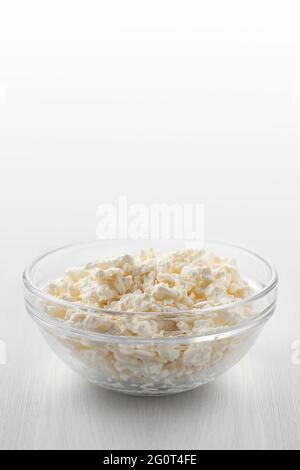 Frischer hausgemachter Bauernhofkäse in einer Glasschüssel auf einem weißen Holztisch. Vertikales Bild Stockfoto