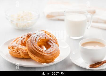 Morgenkaffee mit Kuchen. Puddingringe, Kaffee, Rahm, Quark auf einem weißen Holztisch. Stockfoto