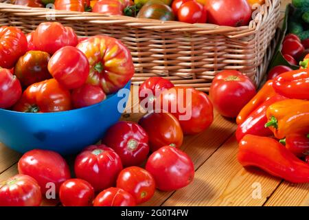 Frische reife natürliche Tomaten und Paprika auf einem Holztisch und in einer Schüssel - Ernte auf dem Bauernhof Stockfoto