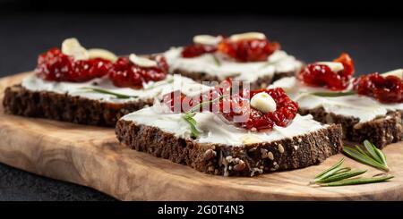 Hausgemachte Mehrkornbrot-Sandwiches mit Frischkäse und getrockneten Tomaten auf einer Holzplatte. Gesunde Ernährung Konzept. Stockfoto