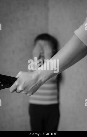 Mama mit Gürtel steht vor dem Kind. Der Sohn weint in der Ecke. Häusliche Gewalt gegen Kinder. Stockfoto