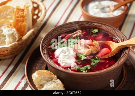 Frisch zubereitetes, warmes, hausgemachtes Borscht: Traditionelles Gericht der russischen und ukrainischen Küche in Steingutgerichten mit Speck, Brot, Sauerrahm und Knoblauch Stockfoto