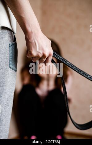 Häusliche Gewalt gegen Kinder. Mama mit Gürtel steht vor dem Kind. Tochter weinte in der Ecke Stockfoto