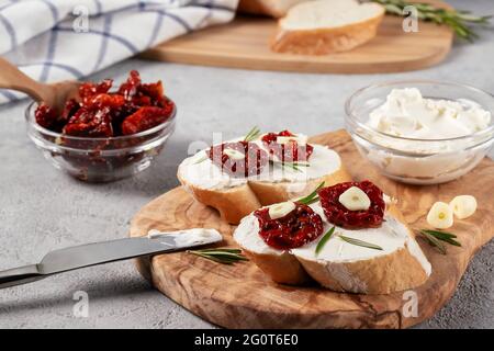 Hausgemachte Sandwiches mit Frischkäse und sonnengetrockneten Tomaten auf einem Holzbrett aus Oliven - leckeres gesundes Frühstück, italienische Küche. Stockfoto