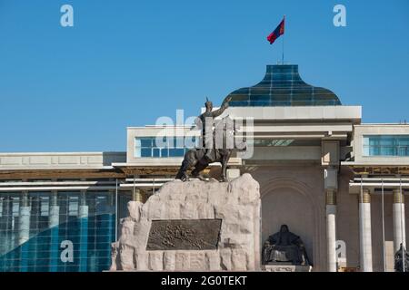 Auf dem Regierungspalast in Ulaanbaatar flattert die mongolische Flagge. Bronzestatue von Sukhbaatar kann auf dem Dschingis Khan Platz gesehen werden. Mongolei Stockfoto