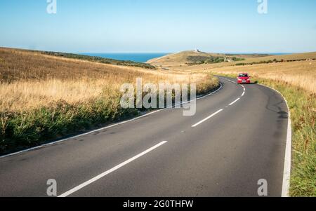 Road Trip Auf Dem Land. Ein Auto, das eine kurvenreiche Straße auf den South Downs, Sussex, England, mit einem Leuchtturm und dem Ärmelkanal in der Ferne fährt. Stockfoto