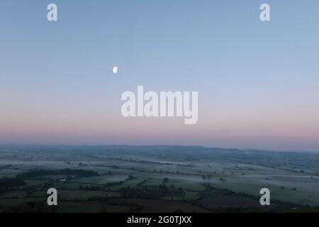 Monduntergang über den Somerset-Levels bei Sonnenaufgang im Mai, vom Glastonbury Tor Stockfoto