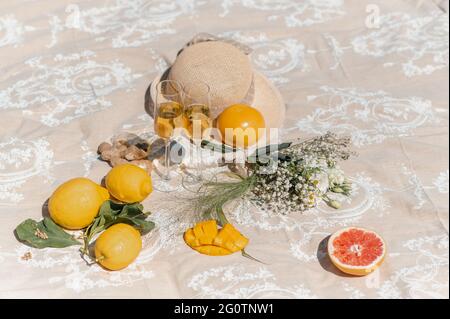 Zwei Weißweingläser auf einer Decke mit Blumen, einem Strohhut und tropischen Früchten. Stockfoto