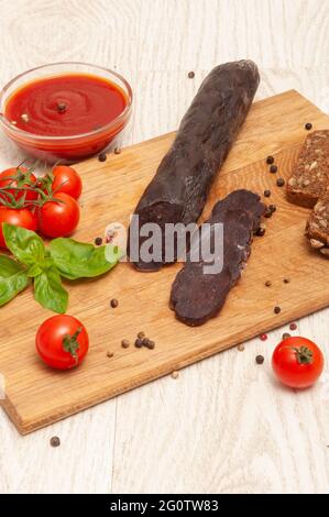 Pferdefleischwurst mit Tomaten und Kräutern auf einem Holzbrett Stockfoto
