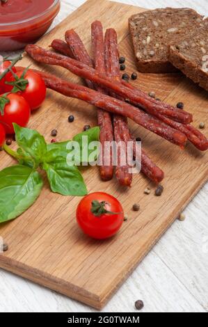 Dünne Würstchen mit Tomaten und Kräutern und schwarzem Brot auf einem Holzbrett Stockfoto