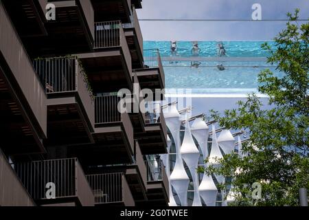 Mit der Architektur der US-Botschaft unten genießen Schwimmer das Wasser des Sky Pools, eines 25 Meter langen, transparenten Wasserpools, der zwei 10-stöckige Wohntürme in 35 Metern Höhe überwindet. Die weltweit größte freistehende Poolstruktur aus Acryl bei der neuen Embassy Gardens-Anlage von Ecoworld Ballymore in Nine Elms am 3. Juni 2021 in London, England. Stockfoto