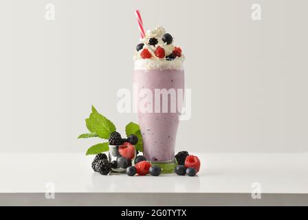 Beerenmilchshake mit Creme verziert mit Brombeeren, Himbeeren und Heidelbeeren auf weißem Holztisch und hellem isolierten Hintergrund. Fron Stockfoto