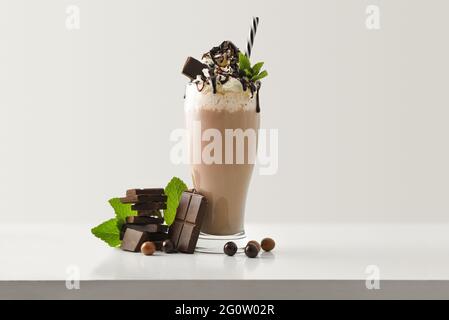 Schokoladenmilchshake mit cremefarbenen Schokoladenportionen und Kugeln auf weißem Holztisch und hellem, isolierten Hintergrund. Vorderansicht. Stockfoto
