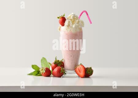 Erdbeer-Milchshake mit cremefarbenem Dekor und Früchten auf weißem Holztisch und hellem, isoliertem Hintergrund. Vorderansicht. Stockfoto