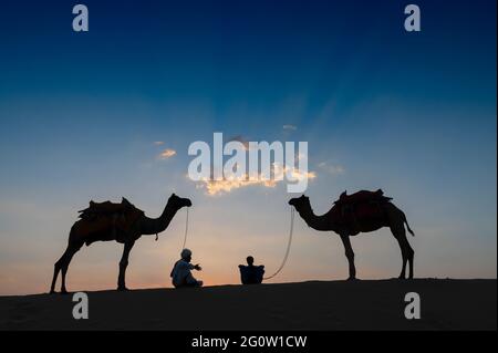 Silhouette von zwei Kamelen und ihre Kamele an den Sanddünen der Thar-Wüste, Rajasthan, Indien. Sonnenuntergang Himmel im Hintergrund. Kameraleuten verdienen ihren Lebensunterhalt. Stockfoto