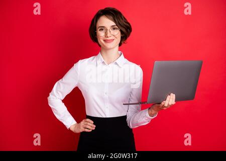 Foto Porträt der Geschäftsfrau halten Laptop lächeln in Brille isoliert hellen roten Hintergrund Stockfoto