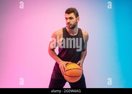 Konzentrierter junger Mann spielt Basketball im Studio Stockfoto