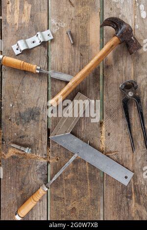 Einige Tischlerwerkzeuge auf einem Holztisch. Es gibt einen Hammer, eine Zange, zwei Meißel, ein Quadrat und Schrauben Stockfoto