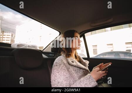 Nachdenkliche Frau mit Smartphone unterwegs im Auto Stockfoto
