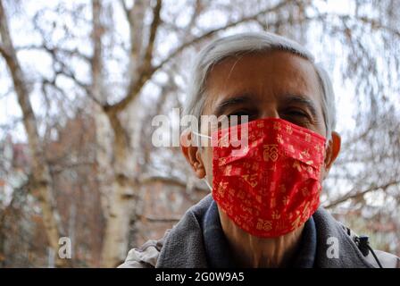 Porträt eines gutaussehenden älteren Mannes trägt eine rote Maske mit chinesischem Glückszeichen in verschiedenen Schriftschnitten. Chinesisches Neujahr 2021. Selektiver Fokus. Stockfoto