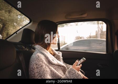 Frau auf der Suche durch das Fenster halten Smartphones im Auto. Stockfoto